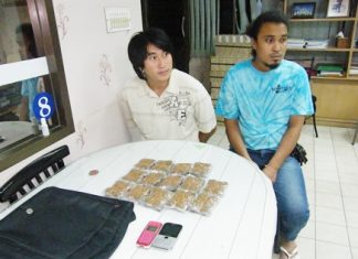 Sinrath Phathasri (left) and Somprasong Chansaard (right) watch as an officer (unseen) weighs one of the packets of marijuana.